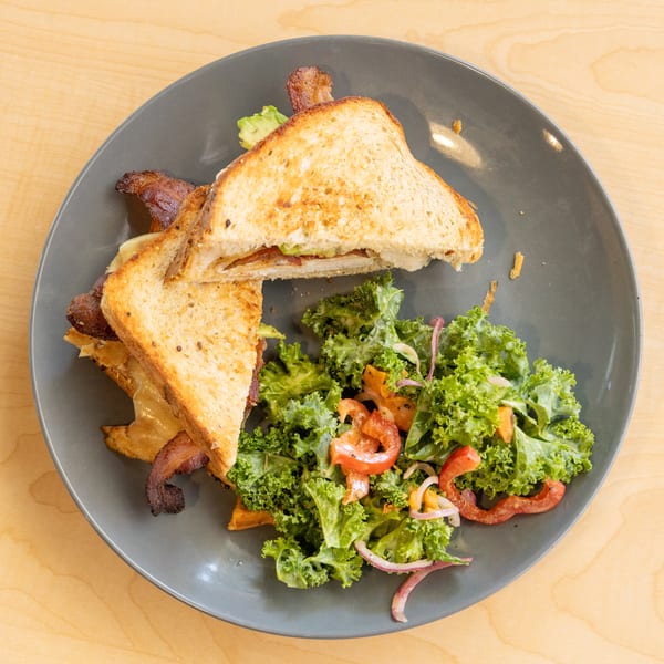 Grilled cheese sandwich with bacon and avocado, served with a side salad on a gray plate.