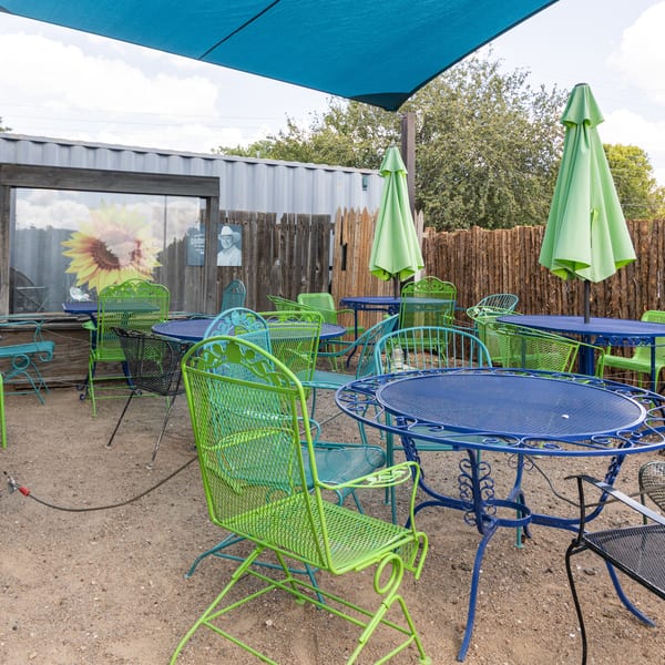 Outdoor patio with blue and green metal tables and chairs under a blue shade sail.