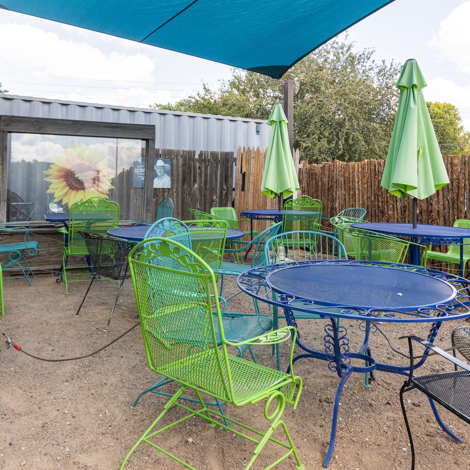 Outdoor patio with blue and green metal tables and chairs under a blue shade sail.
