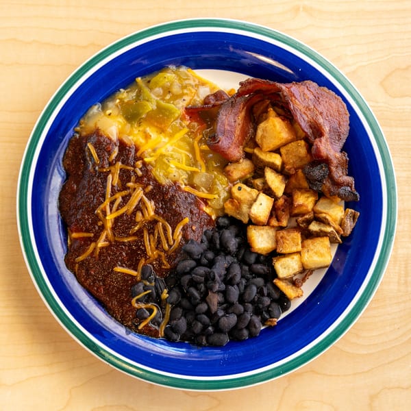A blue plate with green and white trim holds a breakfast of chili, black beans, potatoes, and bacon.