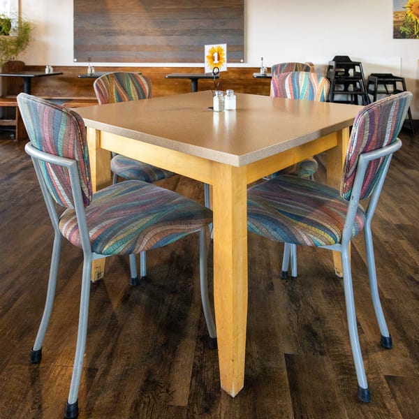 A square wooden table with four chairs featuring colorful striped upholstery in a restaurant dining room.