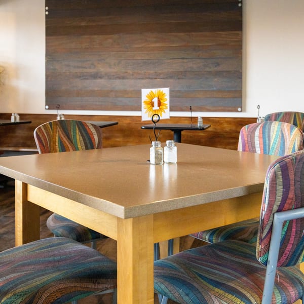 Restaurant dining area with a light brown table, colorful chairs, and a sunflower table number.