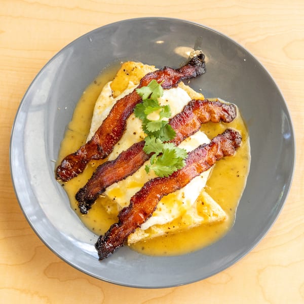 Crispy bacon strips and fried eggs with a yellow sauce and cilantro on a gray plate.