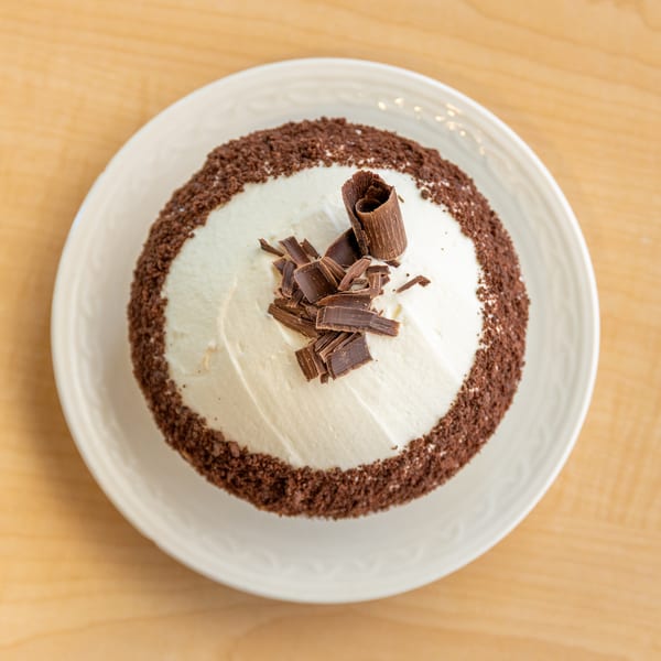 Overhead view of a chocolate cake with white frosting, chocolate shavings, and chocolate crumbs.