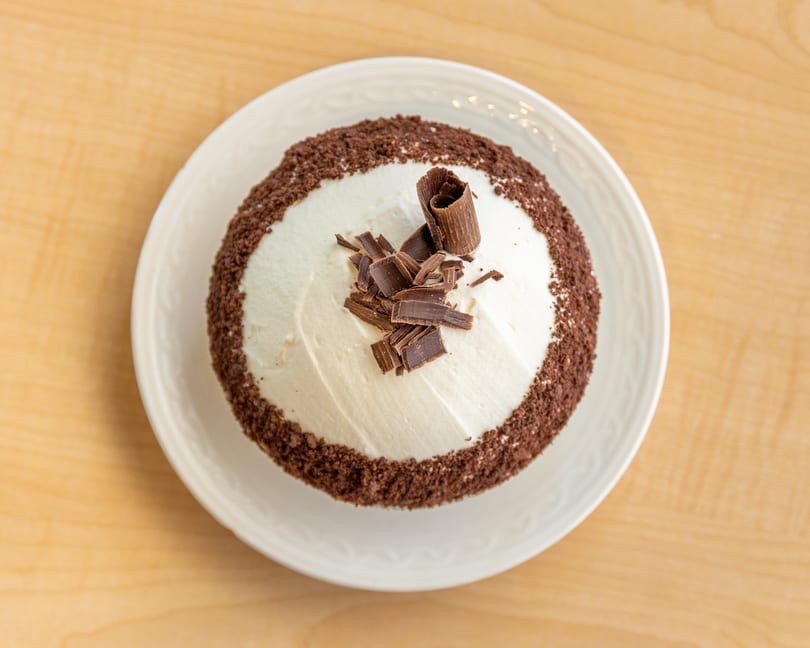 Overhead view of a chocolate cake with white frosting, chocolate shavings, and chocolate crumbs.