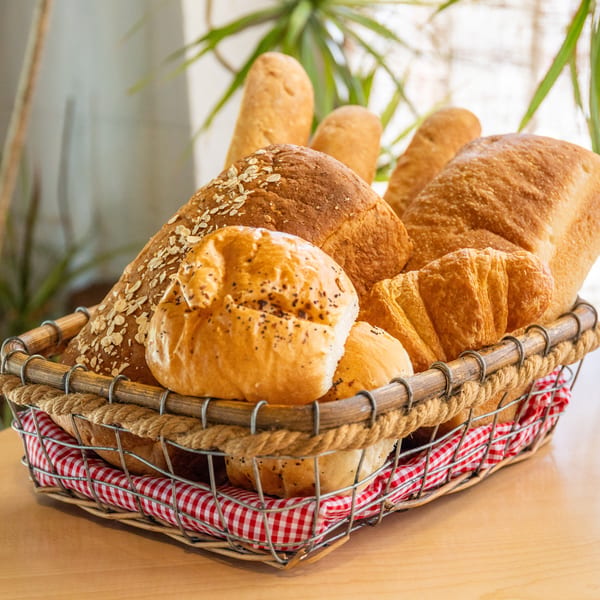 A rustic wire and rope basket filled with various fresh baked breads, rolls, and croissants.