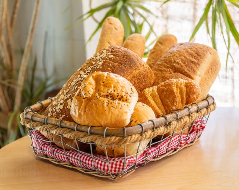 A rustic wire and rope basket filled with various fresh baked breads, rolls, and croissants.
