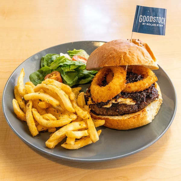 A Goodstock burger with onion rings, fries, and a side salad on a gray plate.