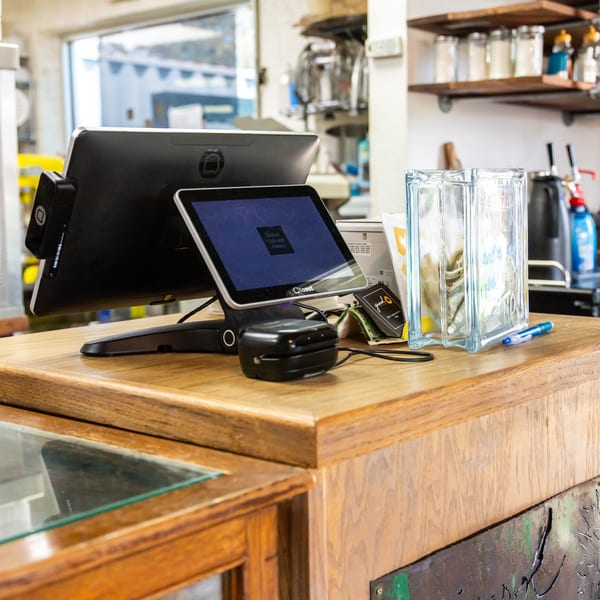 A restaurant counter with two POS screens, a card reader, and a tip jar.