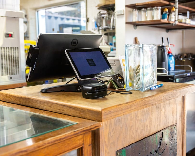 A restaurant counter with two POS screens, a card reader, and a tip jar.
