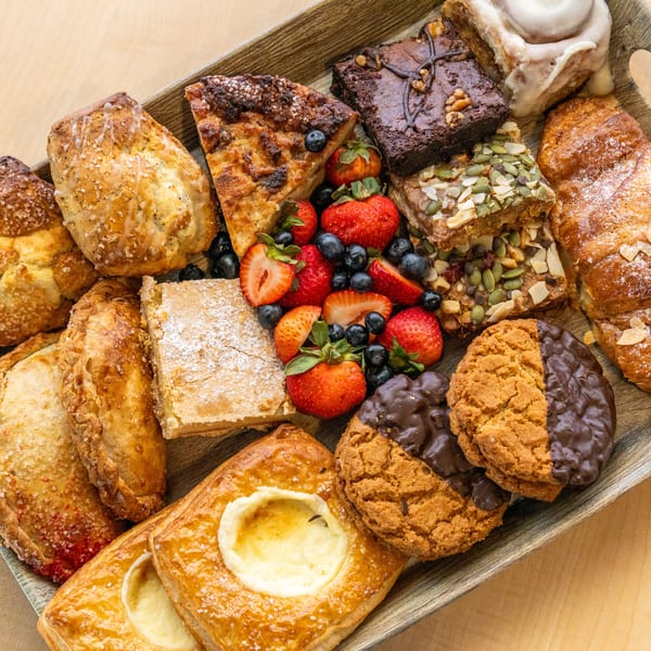 A wooden tray filled with assorted pastries, cookies, brownies, and fresh berries on a light wood surface.