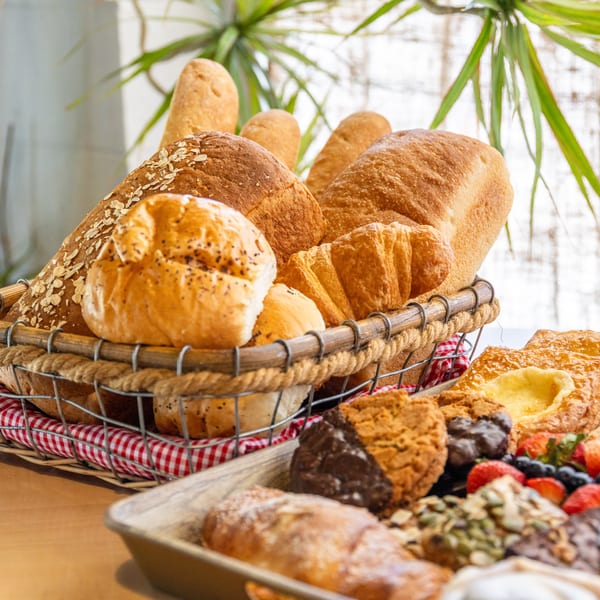 A basket of various fresh breads and pastries, including croissants and rolls, on a wooden table.