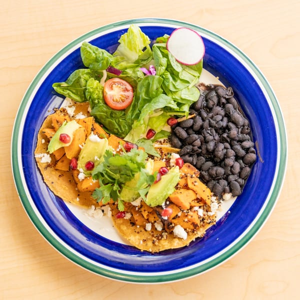A colorful plate of sweet potato tostadas with avocado, black beans, and a side salad.