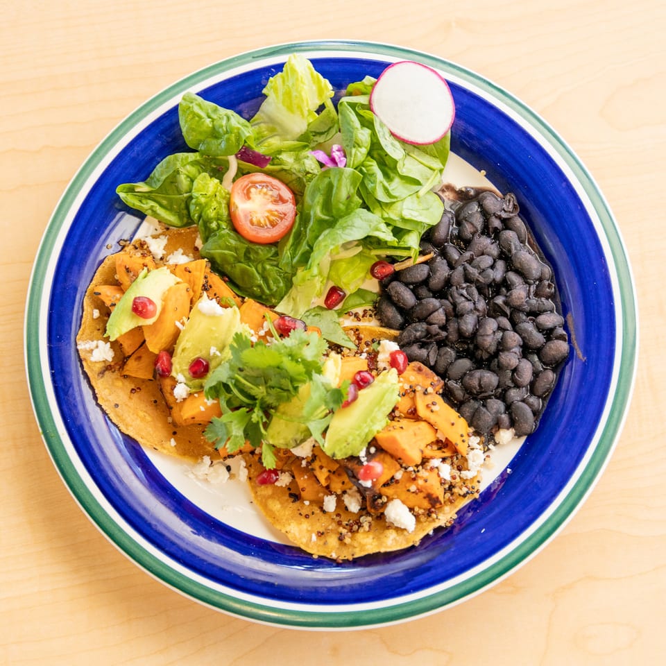 A colorful plate of sweet potato tostadas with avocado, black beans, and a side salad.