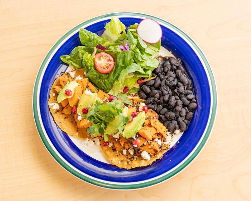 A colorful plate of sweet potato tostadas with avocado, black beans, and a side salad.