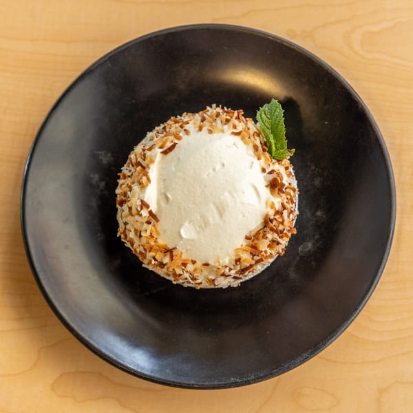 A coconut cream pie with toasted coconut flakes and a mint sprig on a black plate.