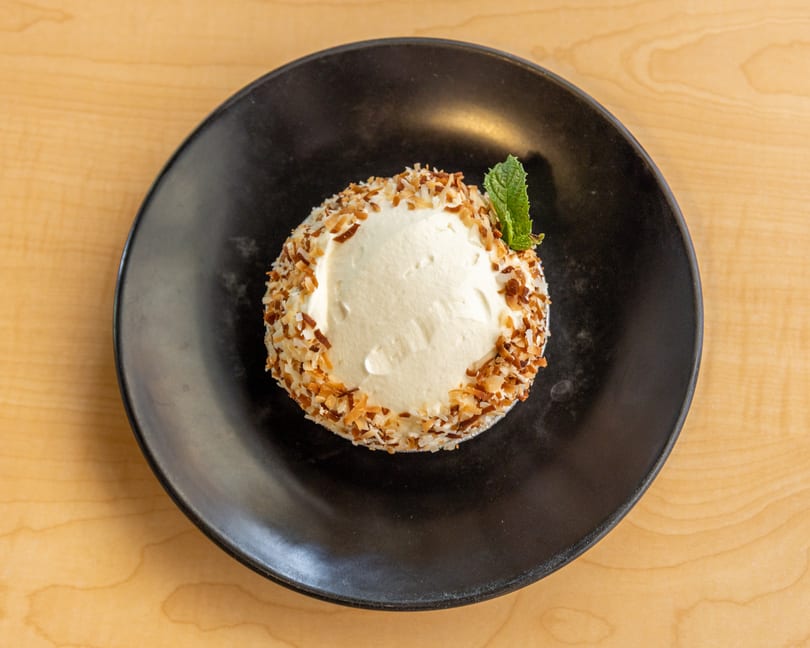A coconut cream pie with toasted coconut flakes and a mint sprig on a black plate.