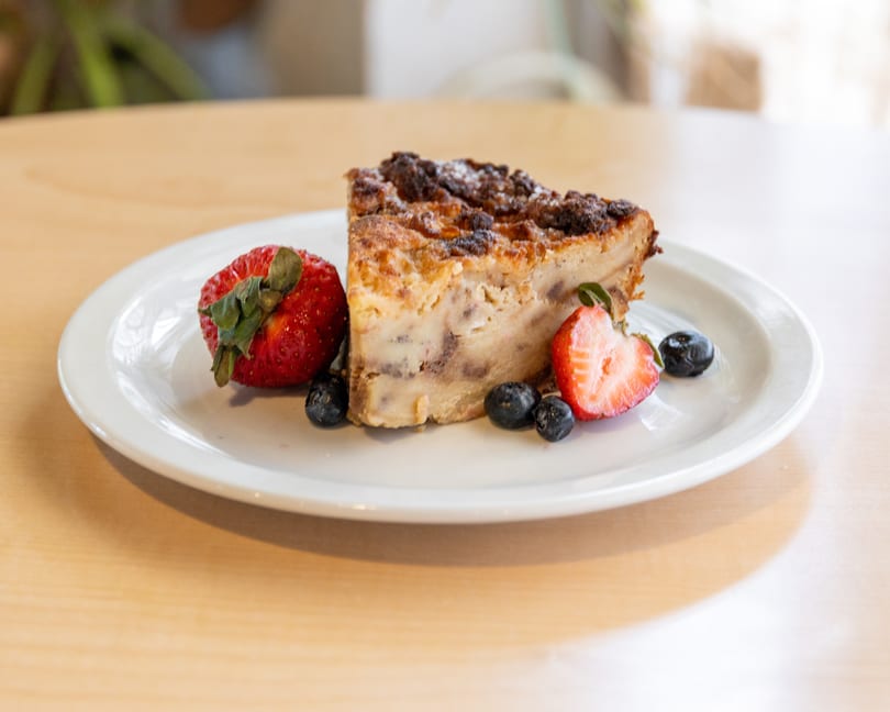 Slice of bread pudding with strawberries and blueberries on a white plate.