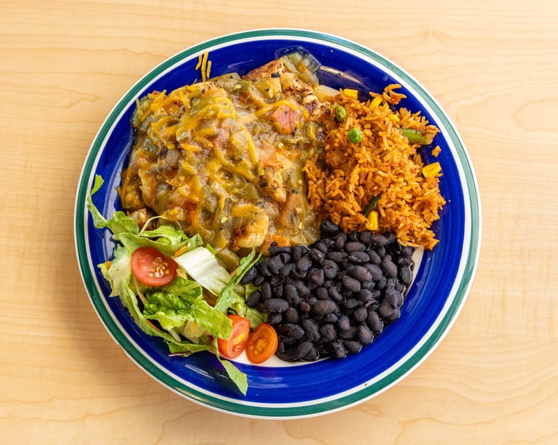 Chicken smothered in green chili sauce with rice, black beans, and a side salad.