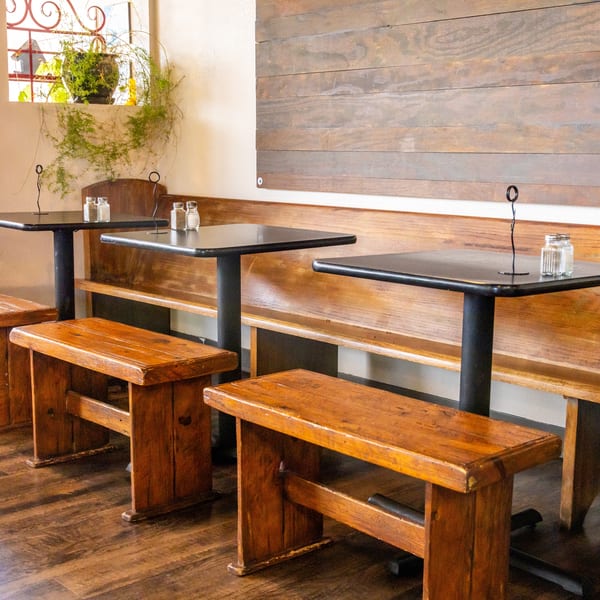 Restaurant interior with dark tables, wooden benches, and a long wooden wall panel.