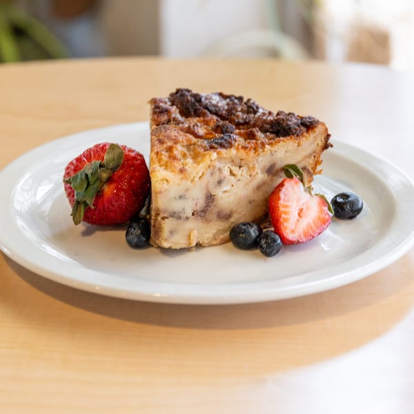 Slice of bread pudding with strawberries and blueberries on a white plate.