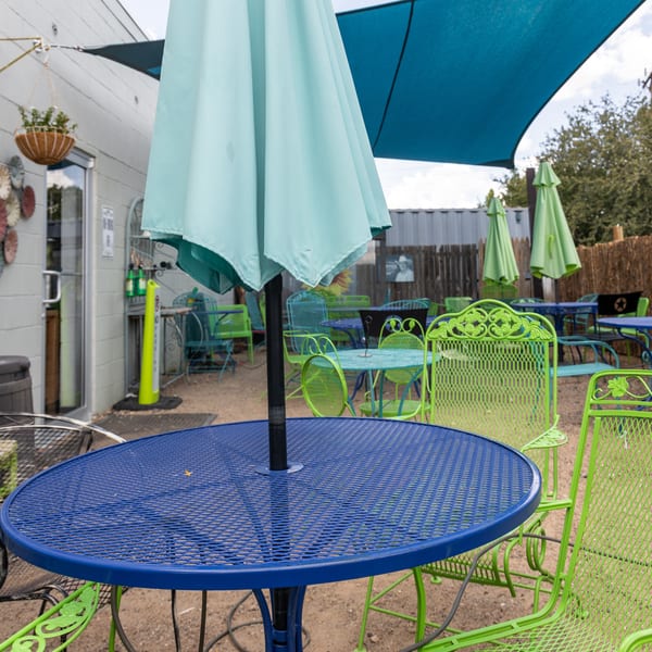 Outdoor patio with blue and lime green metal tables and chairs under a blue shade sail.