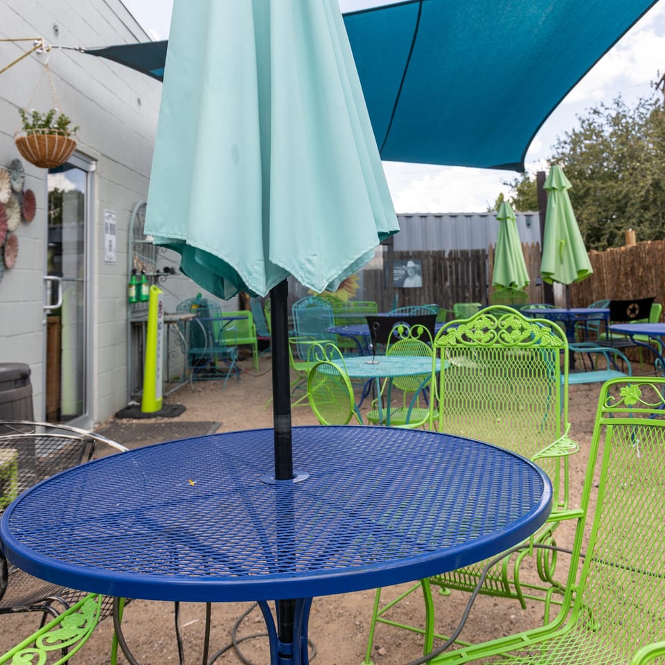 Outdoor patio with blue and lime green metal tables and chairs under a blue shade sail.
