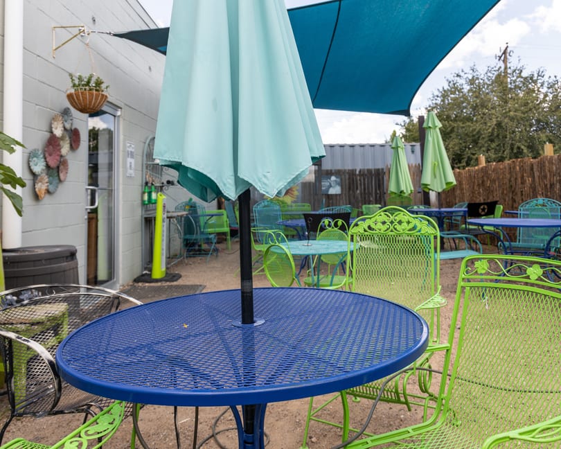 Outdoor patio with blue and lime green metal tables and chairs under a blue shade sail.