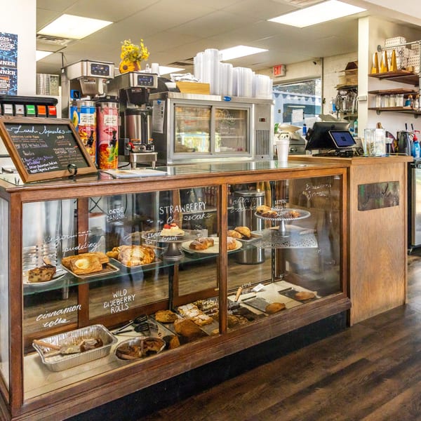 A bakery display case filled with pastries, cakes, and cookies, with a "Lunch Specials" chalkboard.