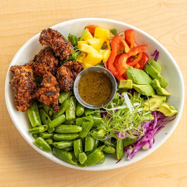 A colorful salad bowl with crispy chicken, mango, bell peppers, avocado, snap peas, and dressing.